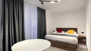 Quarto de hotel moderno com uma mesa redonda, uma cama com cabeceira de madeira e um lustre.