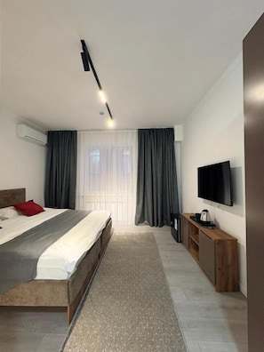 Et moderne hotelværelse med en stor seng, et fladskærms-tv, et trænatbord og en indbygget aircondition.