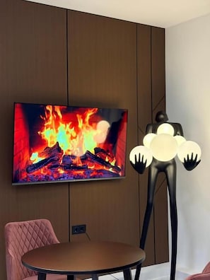 A room with a flat-screen TV mounted on a wall, a round table, and a unique black sculpture with spherical elements. - Avenue Hotel (Almaty)