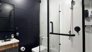 A modern bathroom with a glass-enclosed shower, a toilet, and a sink with a mirror.
