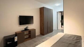 Una habitación de hotel moderna con una cama, un televisor de pantalla plana, un armario y un escritorio con una computadora.