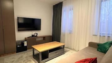 A modern living room with a sofa, a coffee table, a flat-screen TV, and a window with curtains.