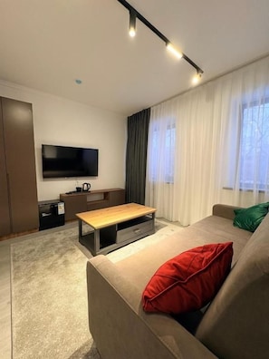 Una sala de estar moderna con sofá, mesa de centro, televisor de pantalla plana y ventana con cortinas.