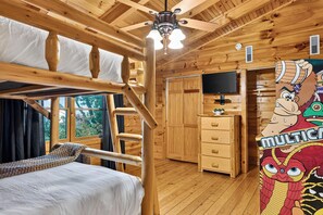 A wooden cabin interior with bunk beds, a ceiling fan, a television, and a wall with cartoon characters. - 5-Acre Smoky Cabin • Hot Tub + Mountain Views • Near Pigeon Forge | Eagle’s View (Sevierville)