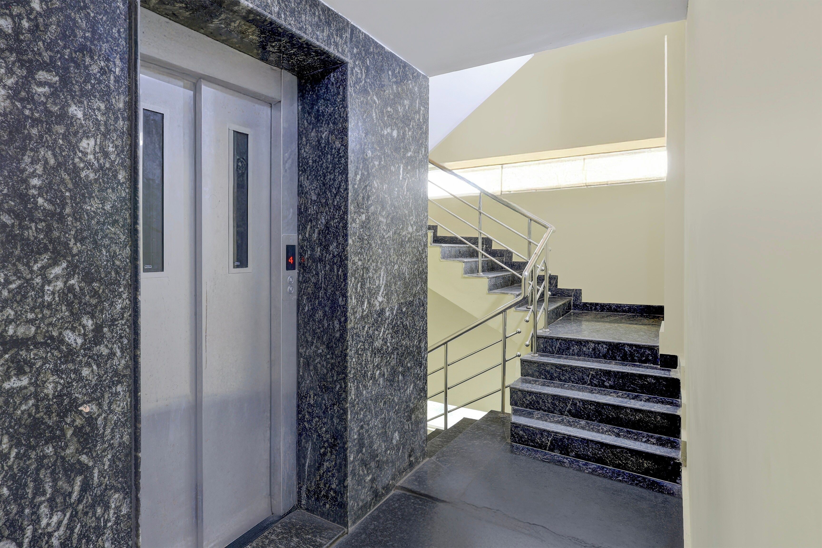 An elevator with a marble wall and a staircase with metal railings.