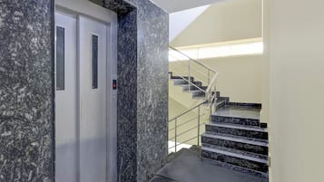 An elevator with a marble wall and a staircase with metal railings.