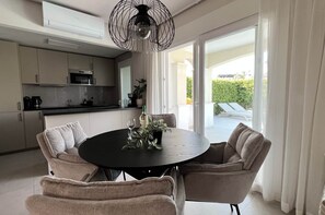 Eine moderne Küche mit Essbereich, inklusive eines runden Tisches mit Stühlen, einer Kaffeemaschine und einem Blumentopf.