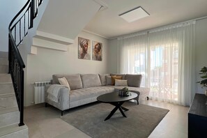 A modern living room with a grey sofa, a coffee table, and a staircase with black railings. - Villa Olivia - Mar Menor Golf Resort (Torre-Pacheco)