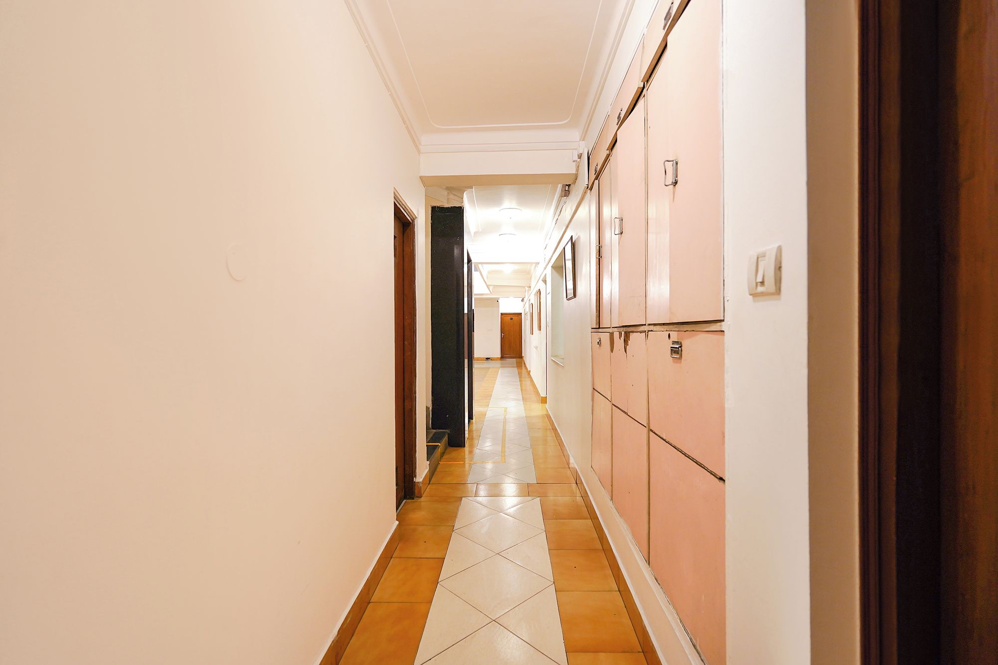 Um corredor com armários de um lado e portas do outro, levando a um espaço no final.