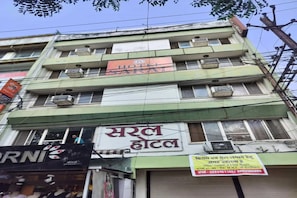 A multi-story building with a hotel sign, air conditioning units, and a storefront with a sign in a local language. - FabHotel Saral (Bhopal)