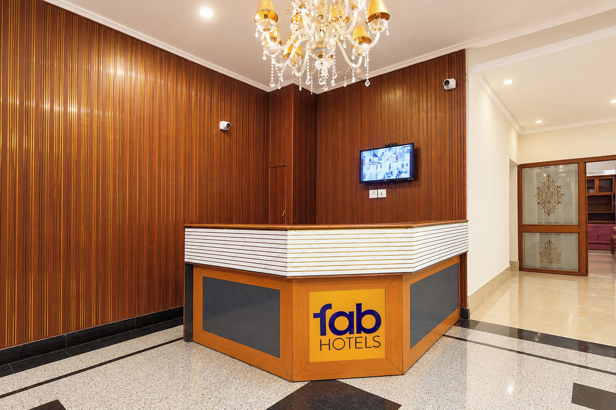Bancada de recepção com acabamento em madeira, um candelabro, uma televisão e uma câmera de segurança.