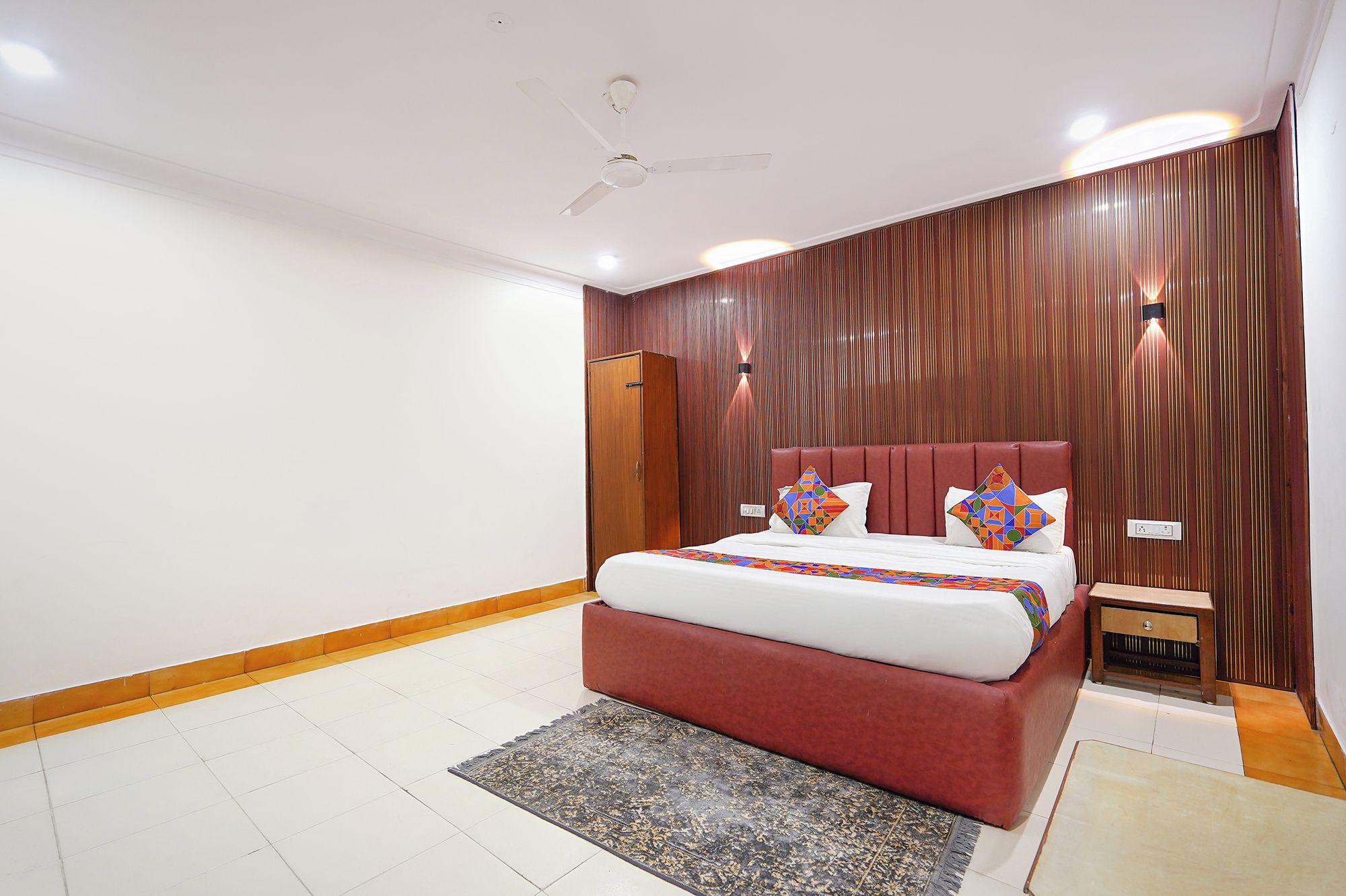 Quarto com cama, ventilador de teto, mesa de cabeceira e guarda-roupa de madeira.