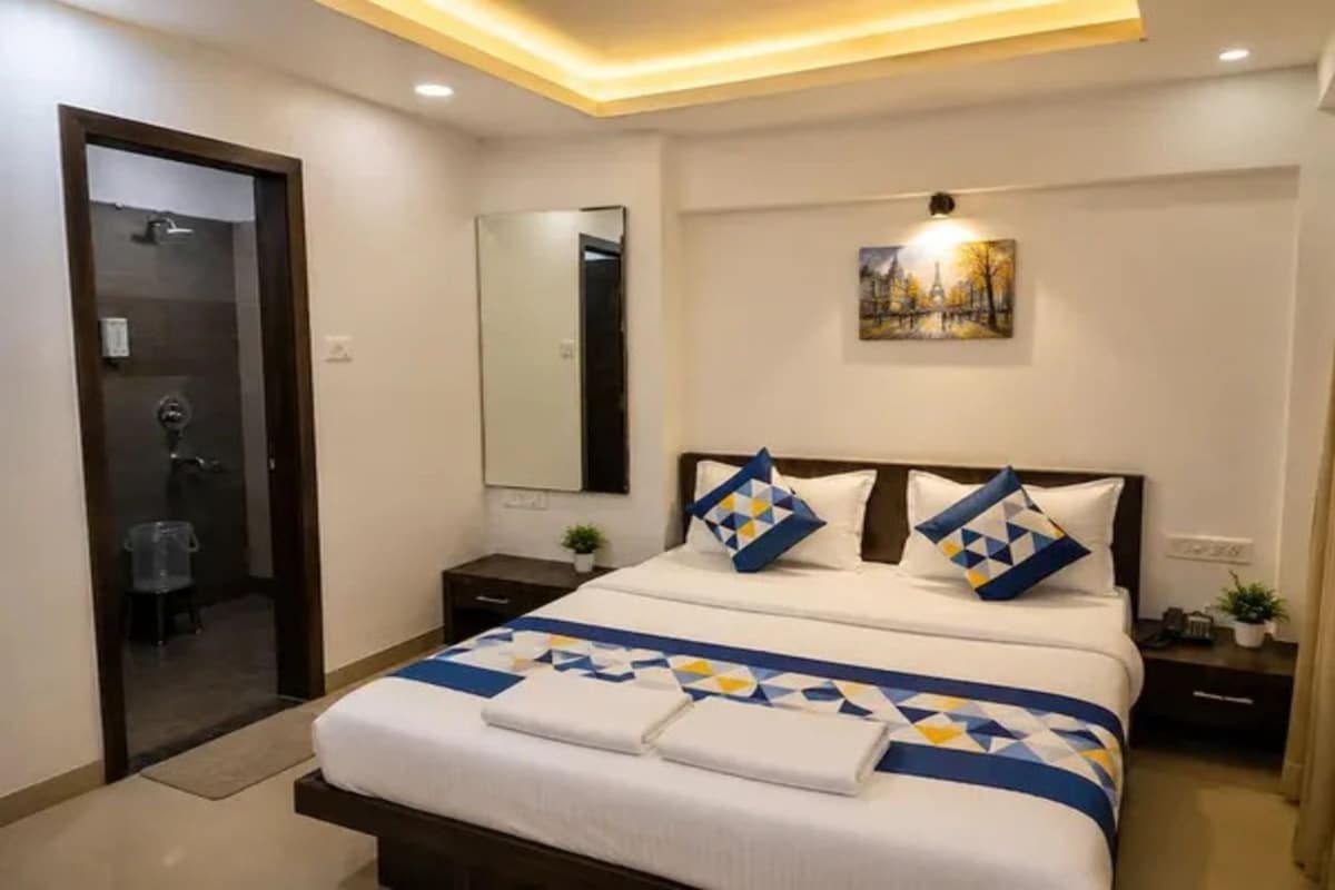 Een hotelkamer met een bed, nachtkastje, spiegel en een schilderij aan de muur.