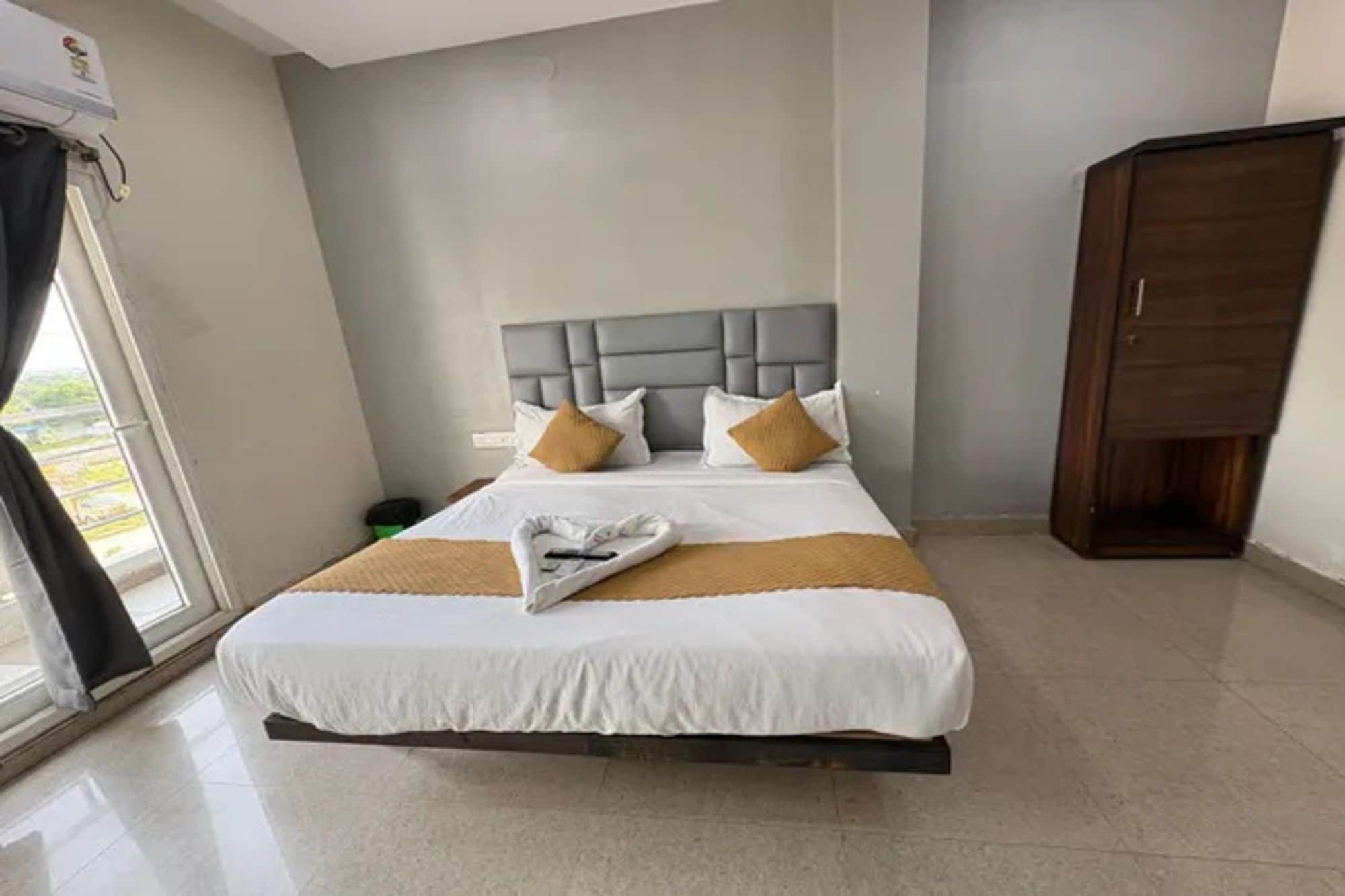 A hotel room with a bed, a headboard, a wardrobe, and a window with curtains.