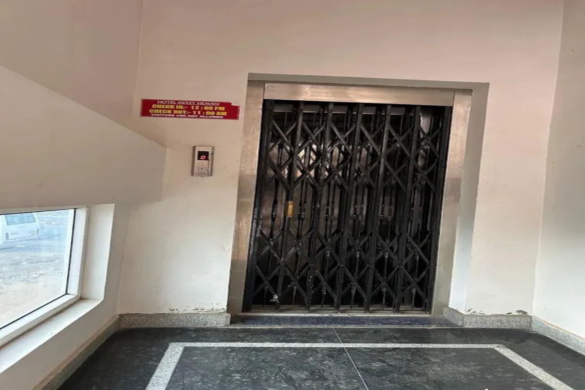 Entrada de hotel con un cartel de recepción, una reja metálica y un teclado digital.