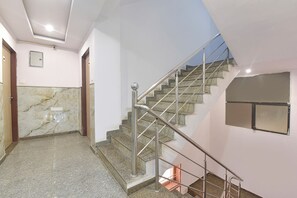 A modern interior with a marble-tiled floor, a staircase with metal railings, and a plain wall with a small window. - FabHotel Sky Blue (Jaipur)
