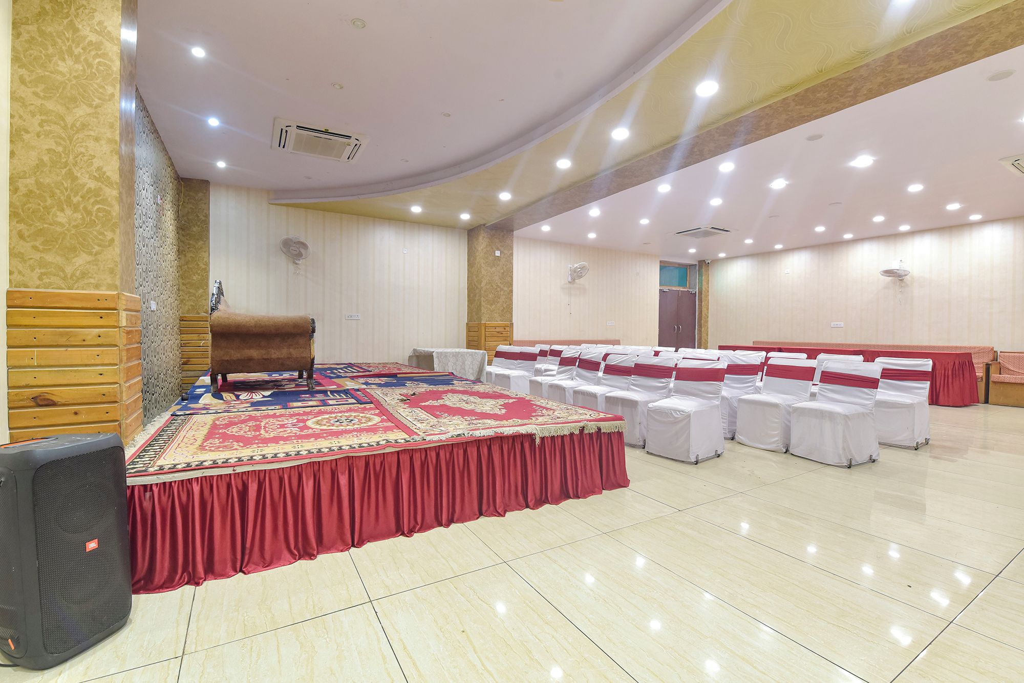 Un salón de conferencias con una gran mesa redonda, sillas blancas con cintas rojas y una alfombra roja.