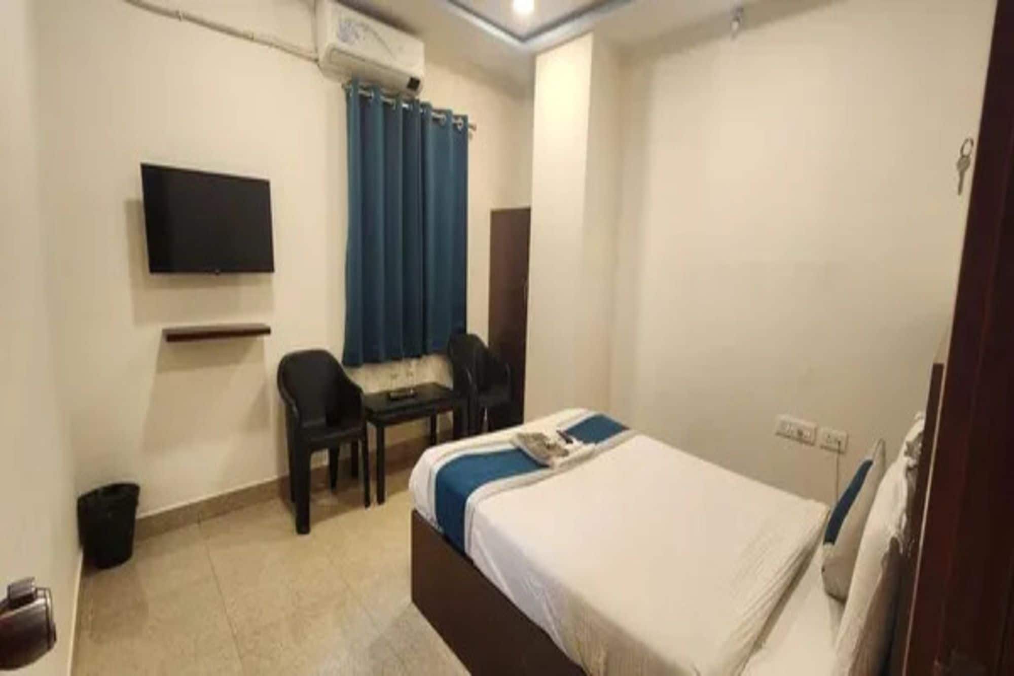 Habitación de hotel con cama, escritorio, silla, televisor y ventana con cortinas.