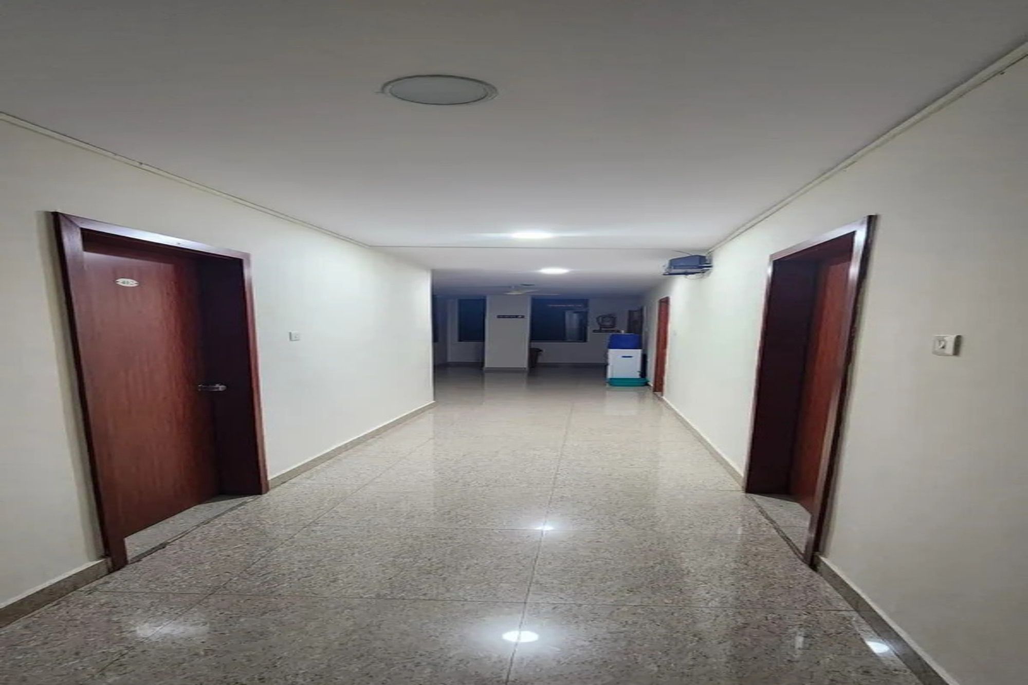 A corridor with doors on both sides, leading to a room with a bed and a window.