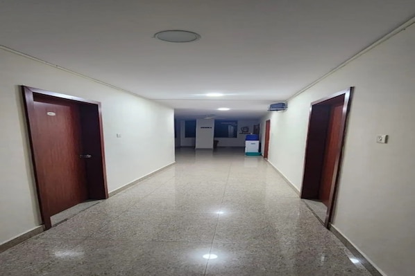 A corridor with doors on both sides, leading to a room with a bed and a window.