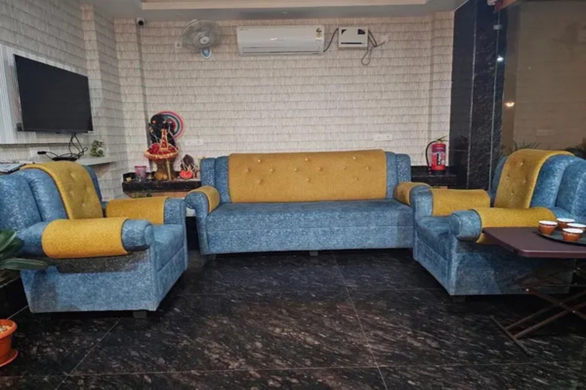 Una sala de estar con un conjunto de sofá, un televisor de pantalla plana montado en la pared y un equipo de aire acondicionado.