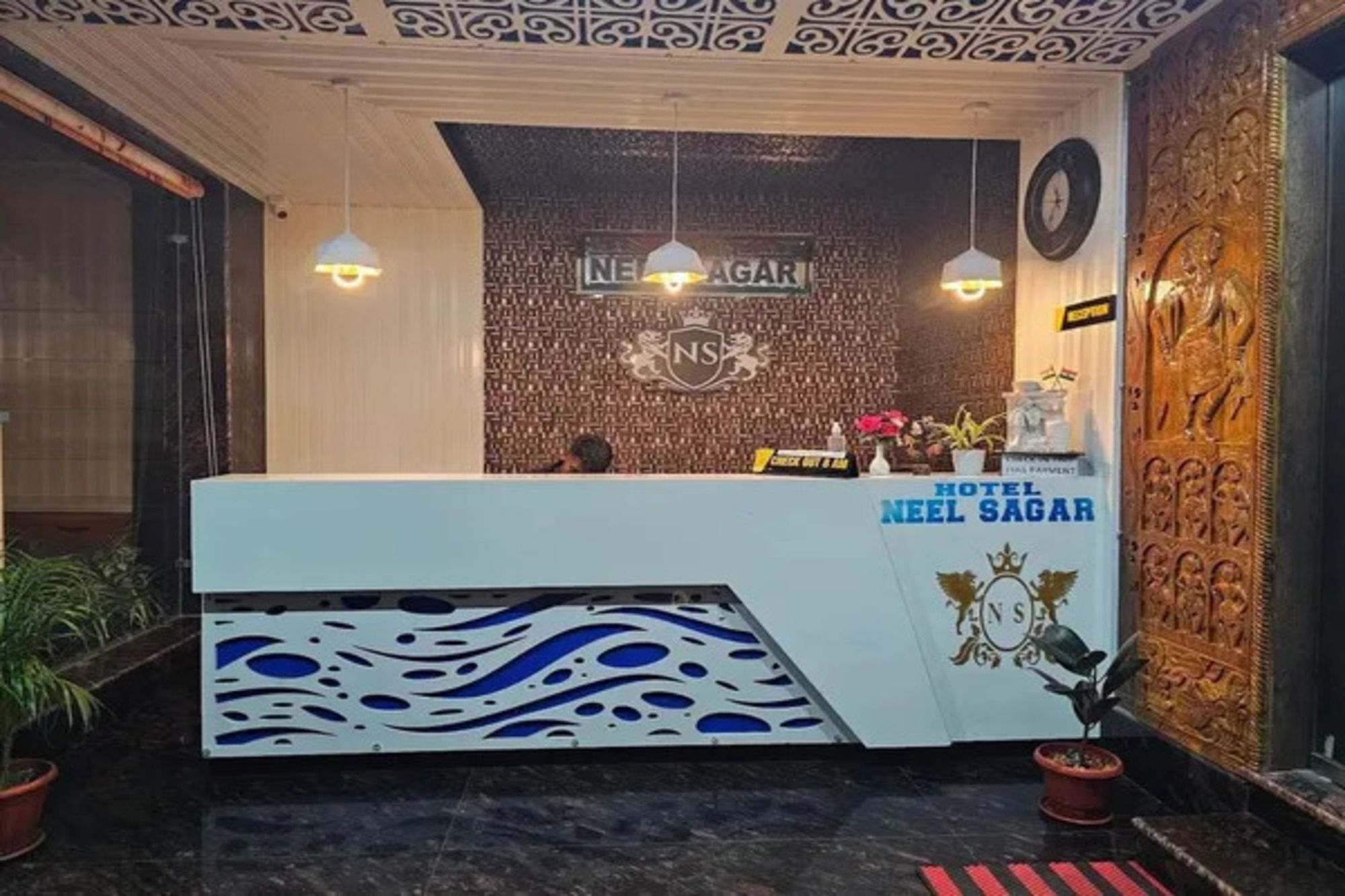 Un mostrador de recepción de hotel con diseño moderno, una zona de registro y una pared decorativa con un logotipo.