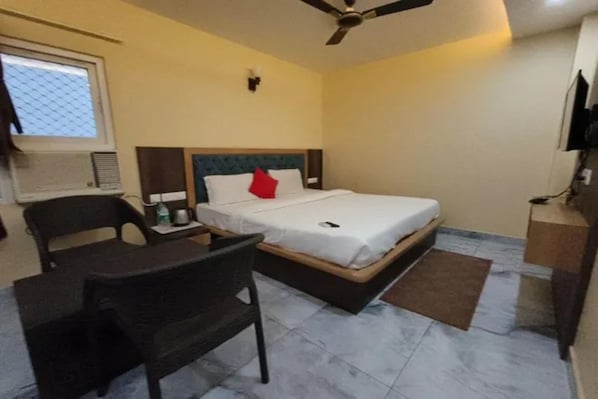 A hotel room with a bed, a desk, a chair, a ceiling fan, and a television.