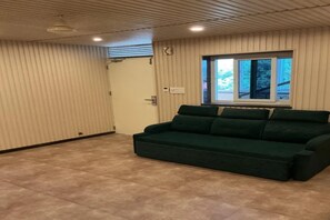 Una habitación con un sofá verde, un ventanal con vistas y una puerta.