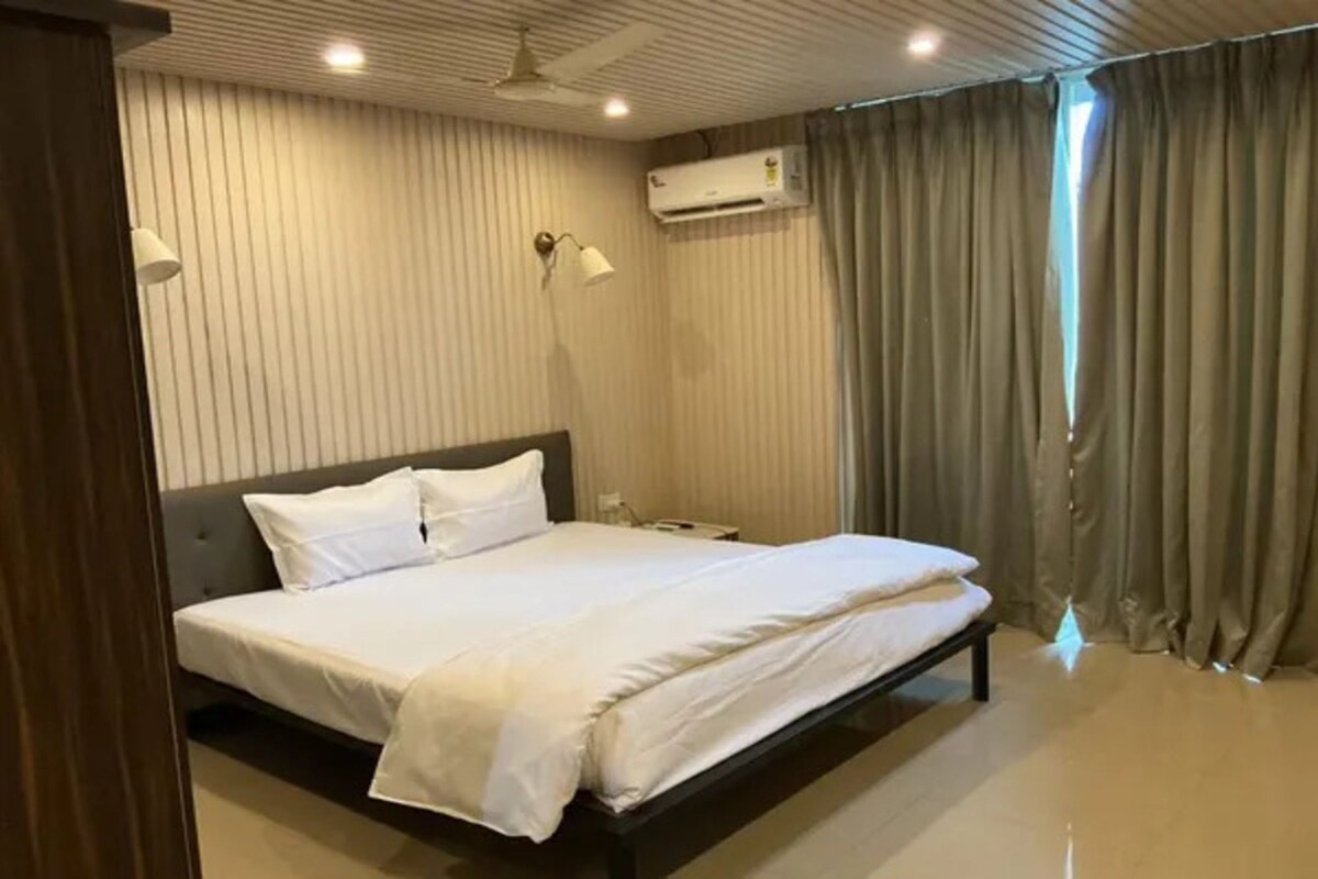 Una habitación de hotel con una cama, un ventilador de techo, un equipo de aire acondicionado y una ventana con cortinas.