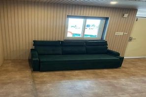 A dark green sofa in a room with vertical paneling on the walls and a window with blinds. - FabHotel Dandelion By The Sea (Panaji)