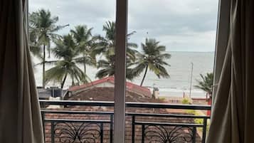 A view from a balcony with a railing, overlooking a beach with palm trees and a cloudy sky.