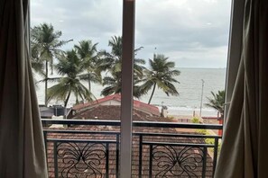 Vista desde un balcón con barandilla, sobre una playa con palmeras y un cielo nublado.