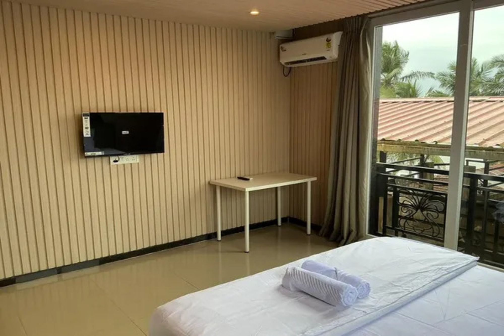 Habitación de hotel con cama, televisor montado en la pared, una mesita y balcón con vistas a palmeras.
