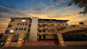 A multi-story hotel with a central entrance, balconies, and a sunset sky.