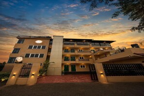 Un hotel de varios pisos con entrada central, balcones y un cielo al atardecer.