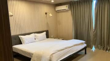 A hotel room with a bed, curtains, an air conditioning unit, and a lamp.