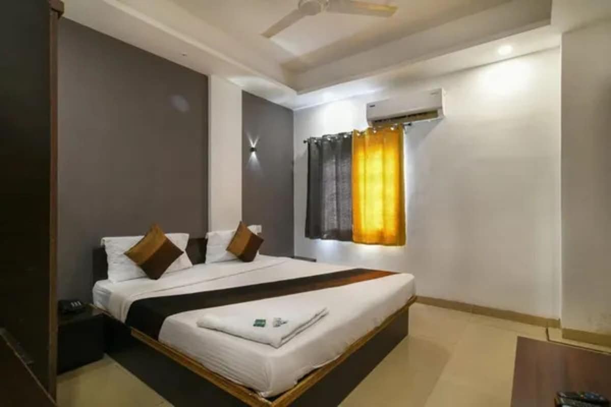 A hotel room with a bed, a bedside table, an air conditioning unit, and a ceiling fan.