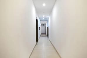 A straight, narrow hallway with white walls and a tiled floor, leading to a door at the end. - FabHotel Aarav 94 (Indore)