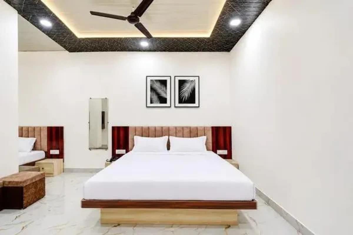 A hotel room with a large bed, a ceiling fan, a wall-mounted air conditioning unit, and two framed pictures on the wall.