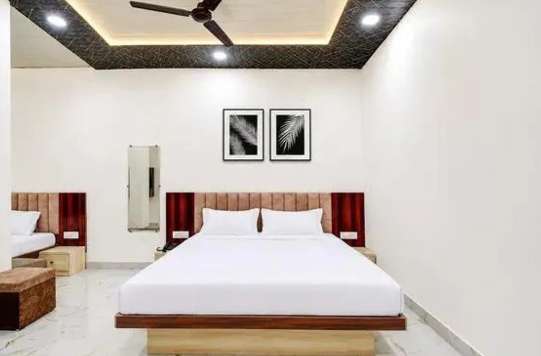 A hotel room with a large bed, a ceiling fan, and two framed pictures on the wall.