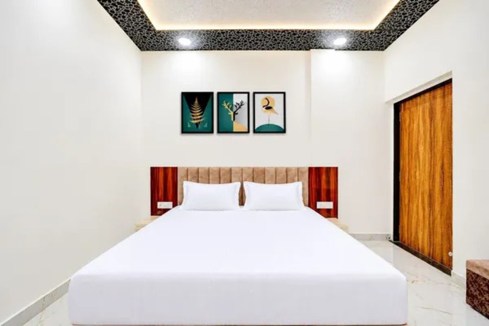 A hotel room with a large bed, a wooden wardrobe, and two framed artworks on the wall.