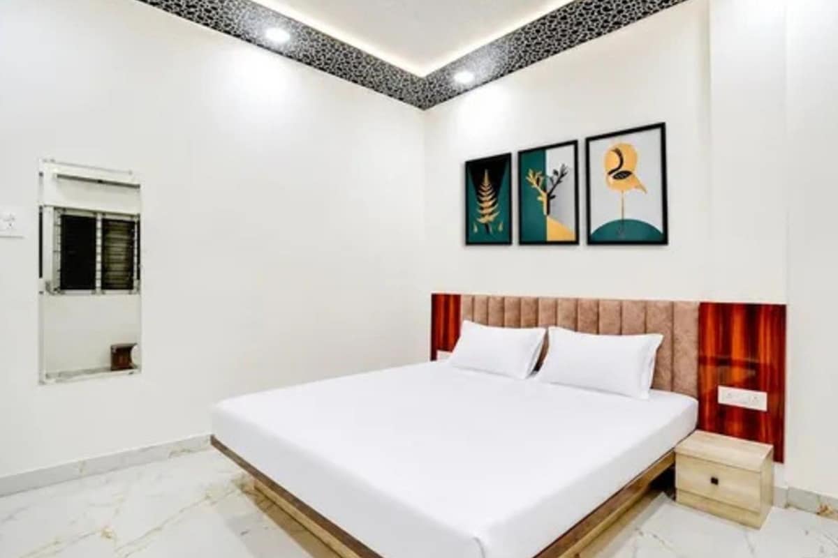 A hotel room with a bed, a nightstand, a mirror, and three wall-mounted artworks.