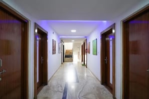Un pasillo con puertas de madera, suelo de mármol y una escalera al fondo.