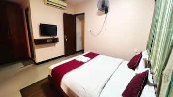 Una habitación de hotel con una cama, un televisor, un equipo de aire acondicionado y un ventilador.