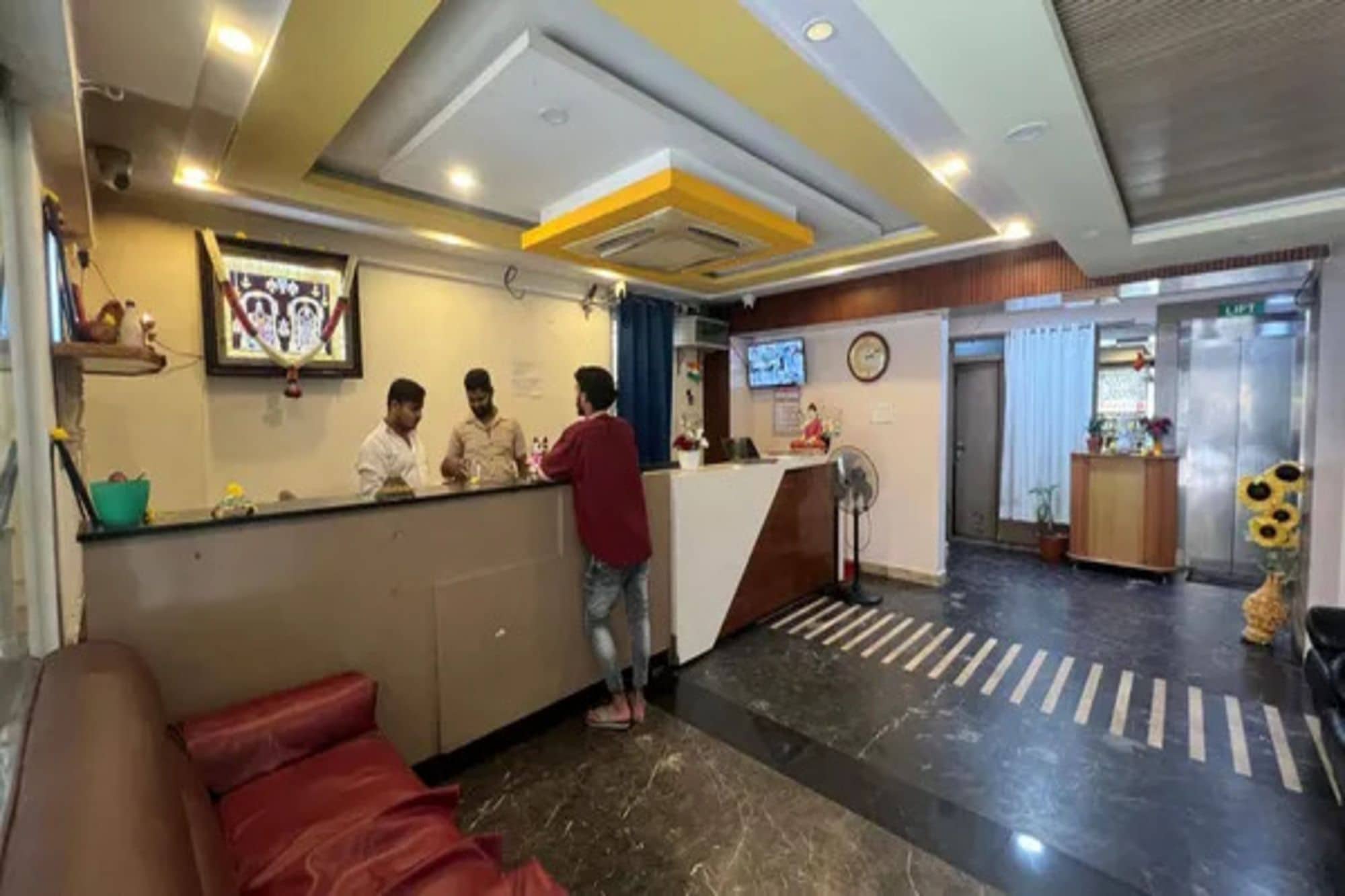 Zona de recepción de hotel con mostrador, área de espera con sofá rojo y un reloj en la pared.