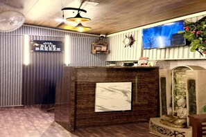 Un espace d’accueil avec un comptoir de réception en bois, un téléviseur fixé au mur et un élément décoratif mural.