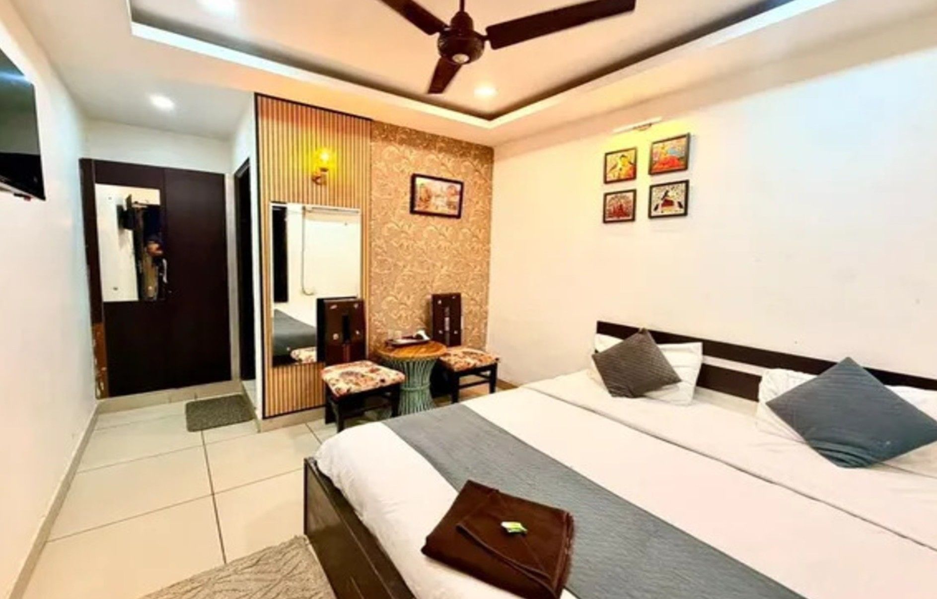 Una habitación de hotel con cama, escritorio, silla, armario y ventilador de techo.