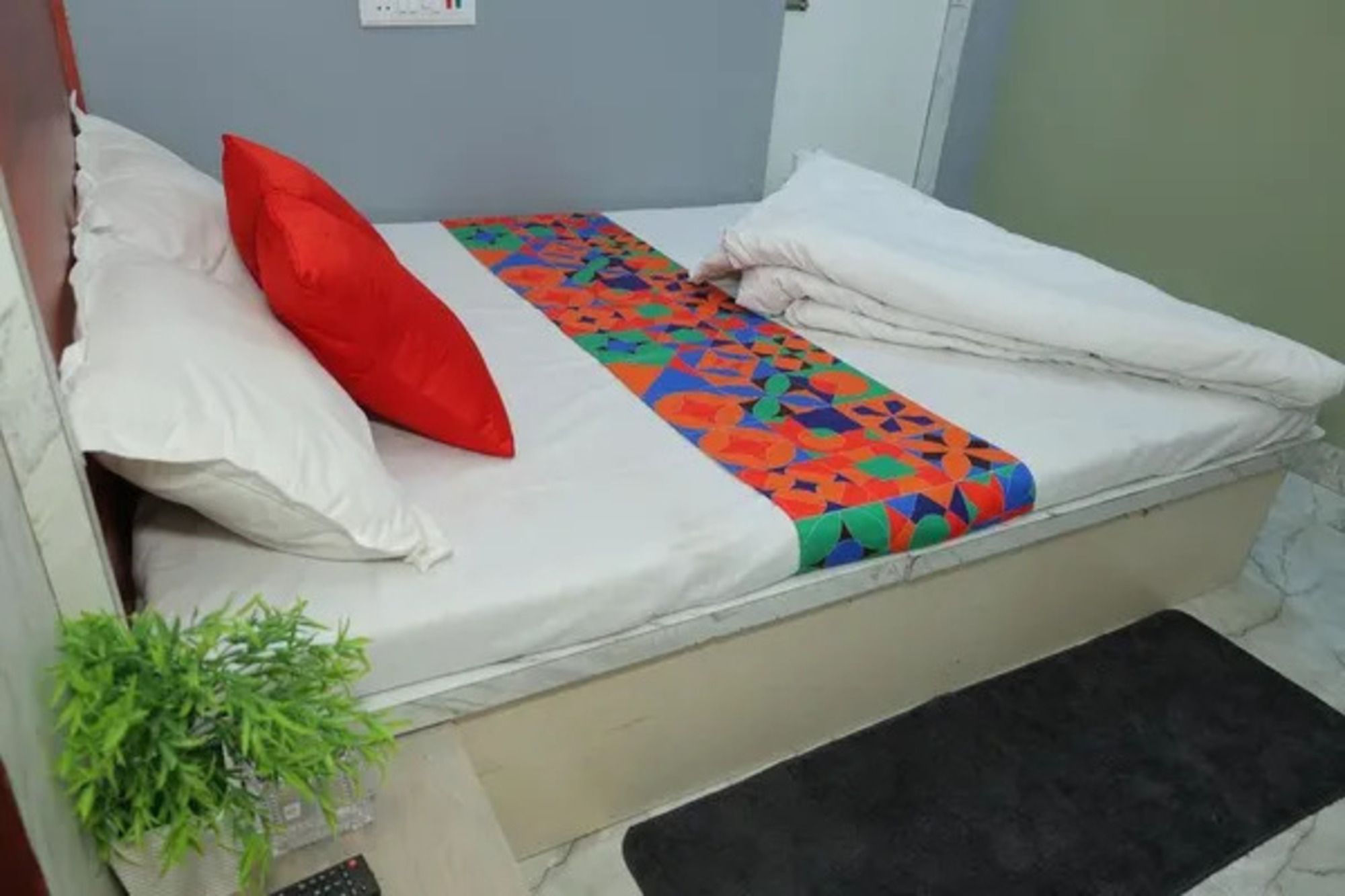 A small bed with a colorful blanket, white pillows, and a small plant beside it.