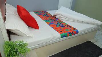 A small bed with a colorful blanket, white pillows, and a small plant beside it.