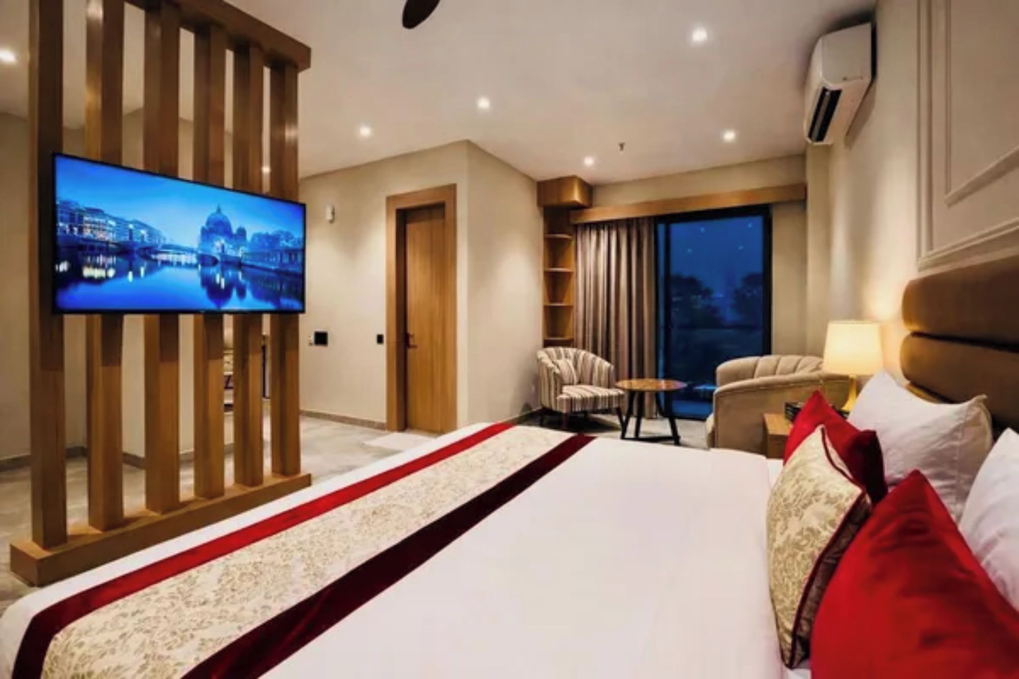 A hotel room with a large bed, a television, a seating area with a chair and table, and a view of the outdoors.